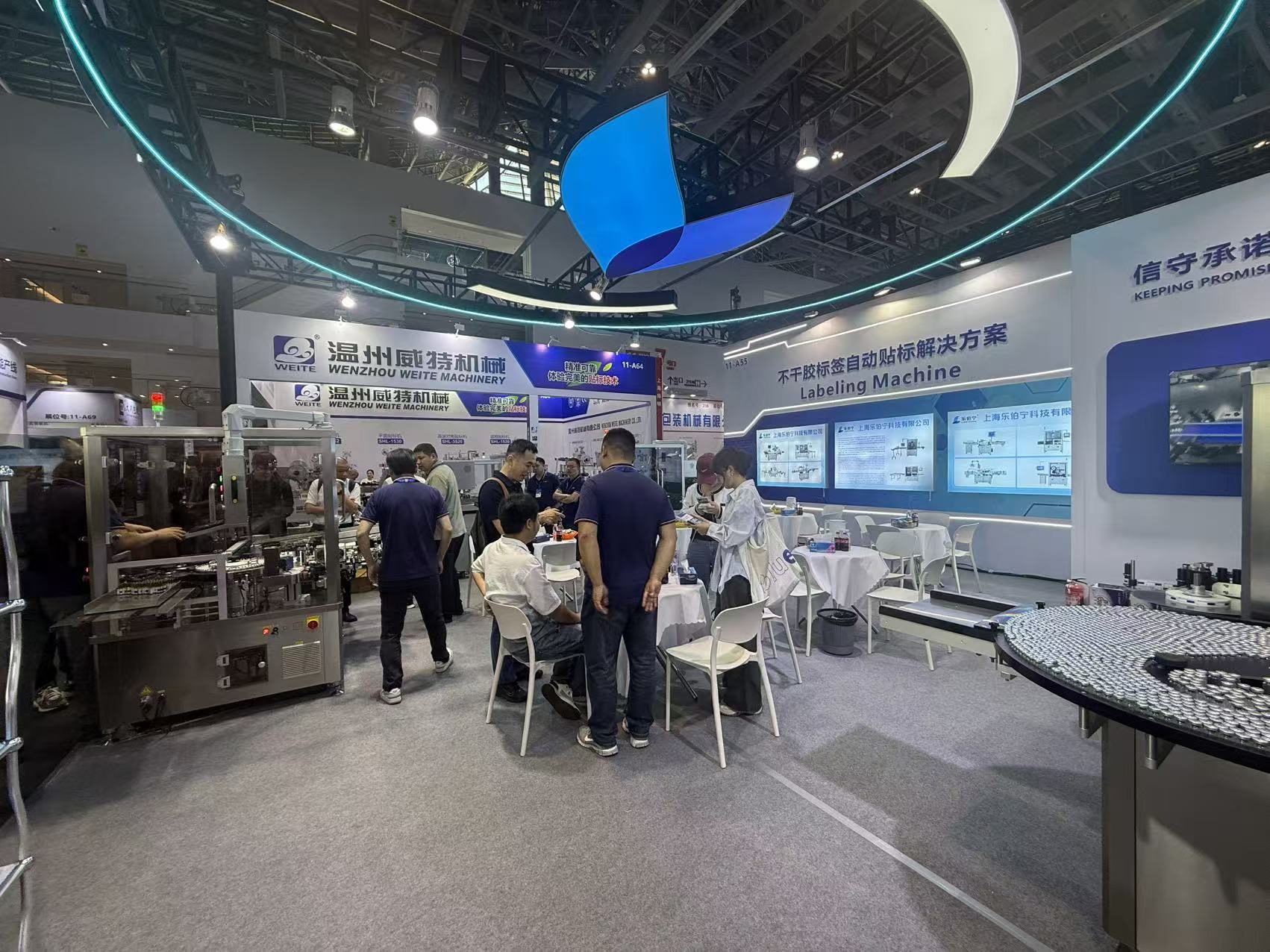 LEBONING team and exhibition visitors gathered between labeling equipment and meeting tables